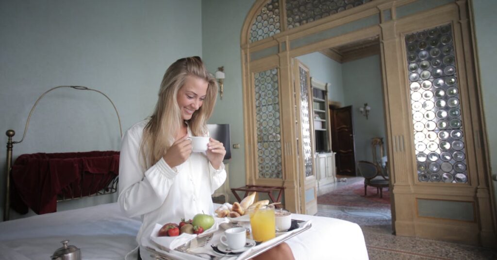 Smiling woman enjoys breakfast in a comfortable, luxurious bedroom setting.